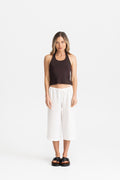 A woman wearing a dark brown modal halter crop top and white wide-leg cropped pants with black slide sandals.