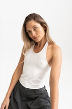 A woman wearing a fitted white modal tank top and dark grey trousers.