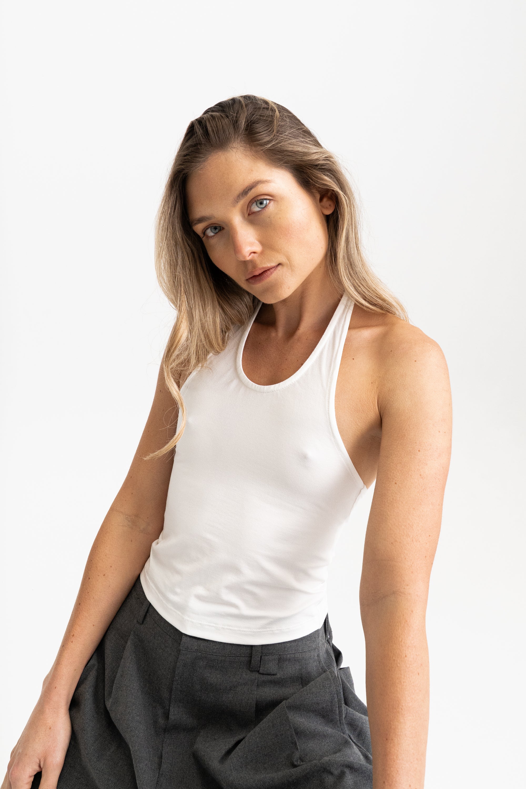 A woman wearing a fitted white modal tank top and dark grey trousers.