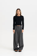 A woman modeling a black long-sleeve cardigan top and dark gray wide-leg trousers against a plain white studio background.