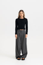 A woman modeling a black long-sleeve cardigan top and dark gray wide-leg trousers against a plain white studio background.