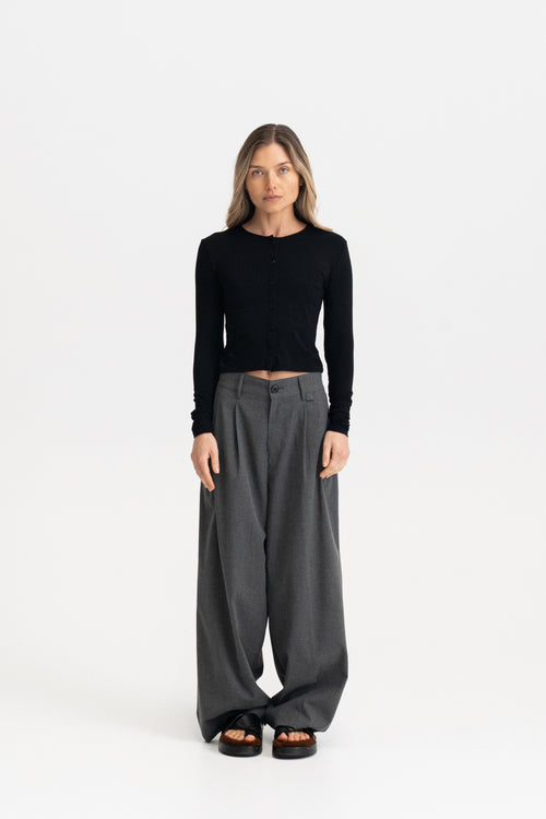 A woman modeling a black long-sleeve cardigan top and dark gray wide-leg trousers against a plain white studio background.